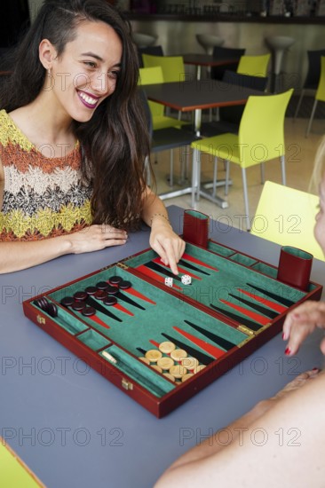 Mother and daughter engaged in a friendly game of backgammon at a cafe, The vibrant setting adds