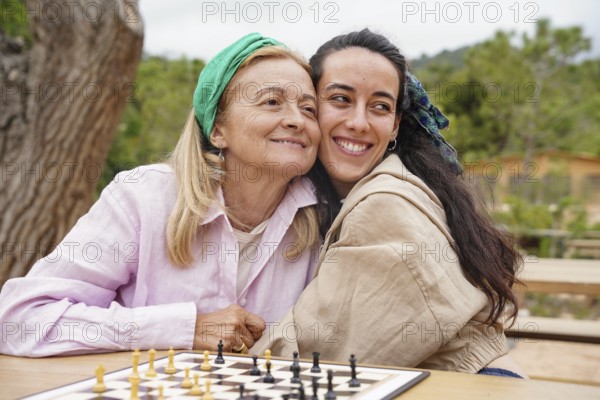 Mother and daughter enjoy a sunny day playing chess outside, sharing a joyful bonding moment The