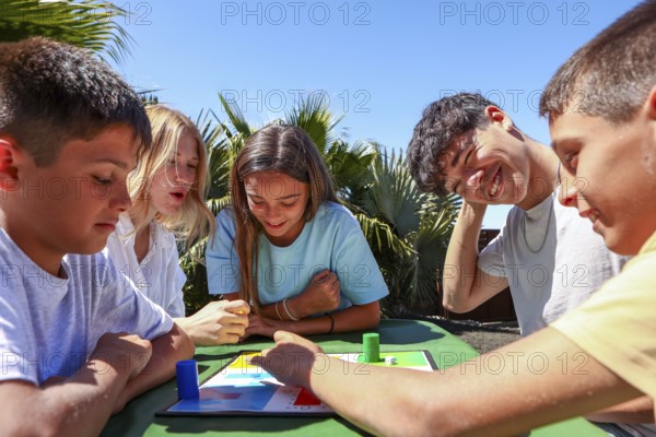 Two older siblings, a young man and woman, enjoy a board game outside with their younger triplets