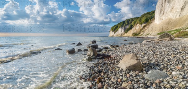 Chalk cliffs and rocky beach with boulders on the Baltic Sea under blue sky with cumulus clouds,