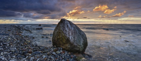 Rocky beach with boulders on the Baltic Sea at sunrise under dark skies with dramatic clouds,