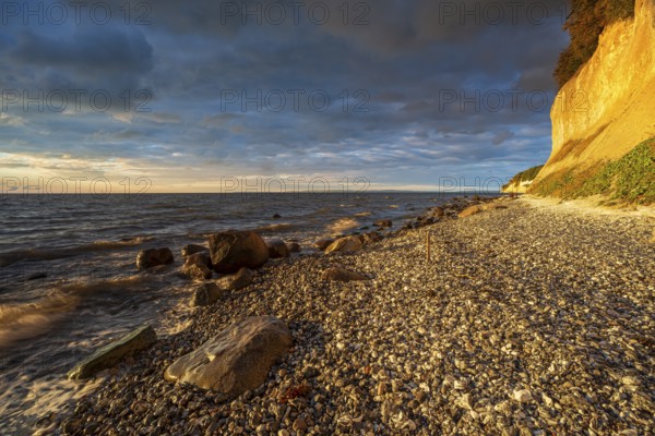 Chalk cliffs and rocky beach with boulders on the Baltic Sea in morning light under dark sky with