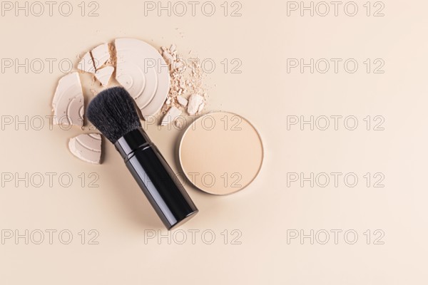 Top view of a makeup brush alongside a compact face powder and broken pieces of a loose powder