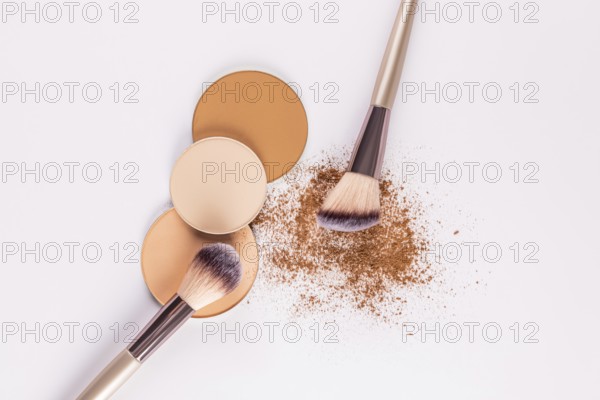Top view of various shades of compact powders next to a makeup brush, with loose powder scattered