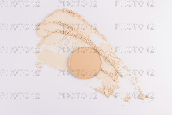 Top view of a circular compact powder alongside scattered loose face powder on a clean, white