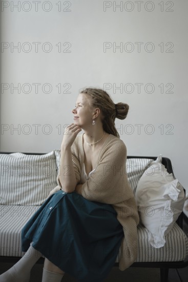 A serene woman sits thoughtfully on a striped sofa, wearing a cozy cardigan and skirt The calm
