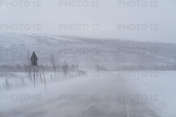 A blizzard envelops a remote road in Swedish Lapland, obscuring distant snow-covered hills and