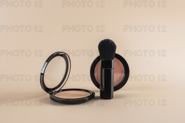 Open compact powder alongside a professional makeup brush, creatively arranged against a soft beige