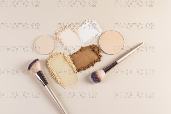 Top view of compact and loose face powders scattered artistically next to makeup brushes on a beige