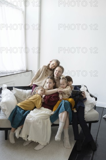 A large family sits together on a sofa in a cozy, bright living room They appear relaxed and