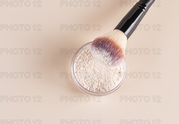 Top view of a makeup brush with pink and white bristles partially dipped into loose face powder,