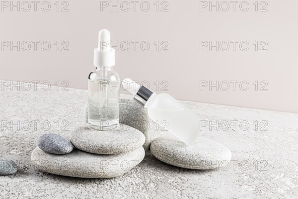 Two glass dropper bottles with clear and frosted finishes are placed elegantly on a stack of