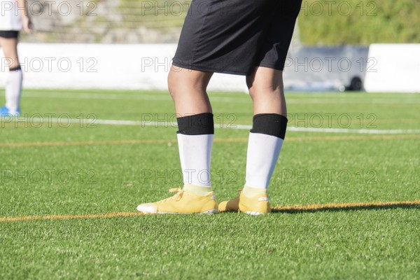 A soccer player stands on a vibrant green soccer field, wearing yellow cleats, black shorts, and