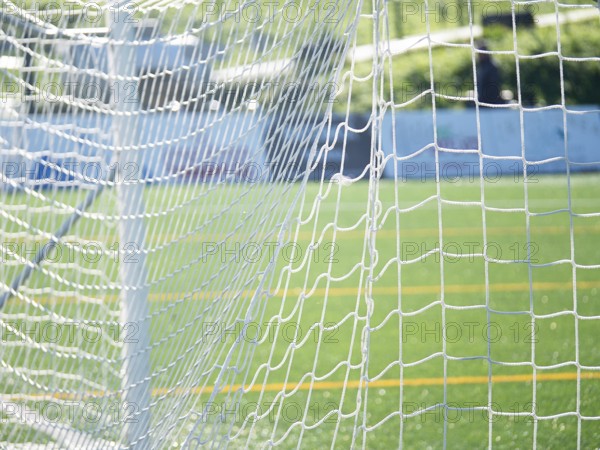Close-up of a soccer goal net with a focus on the grid pattern under bright sunlight. Blurred green