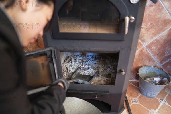 Cropped blurred Asian woman, looking down, is cleaning the ashes from a wood burning stove, holding
