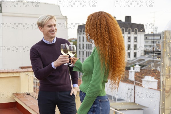Two friends share a cheerful moment, toasting with glasses of white wine on a rooftop The urban