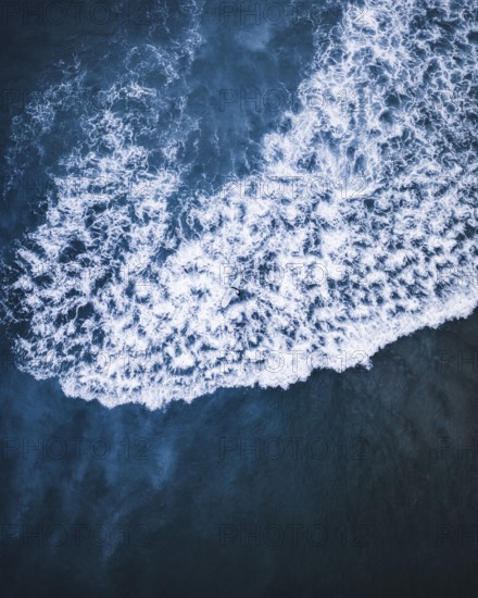 A breathtaking aerial shot of white ocean waves crashing against deep blue waters on the coast of