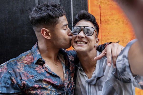 Latin gay couple taking selfie while embracing warmly. One partner kisses the other's cheek, while