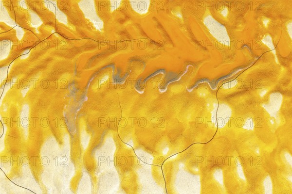 Vivid golden mud flows on a cracked, textured surface, creating an abstract and visually striking