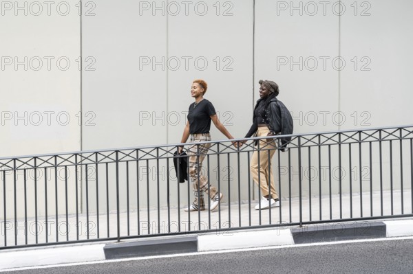 Two people walk hand in hand, smiling outdoors, expressing love and unity as a multiethnic couple.
