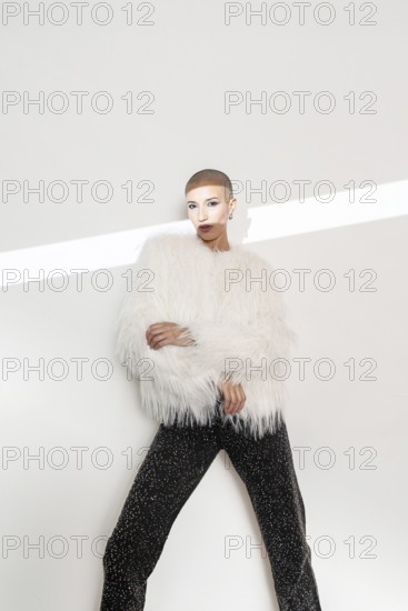 Middle aged woman with a shaved head wears a fluffy white sweater and sparkly black pants. She