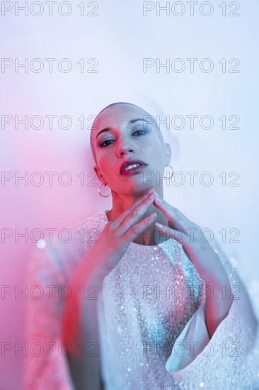 Middle-aged woman with shaved head in stylish pose, adorned with intricate attire. Artistic