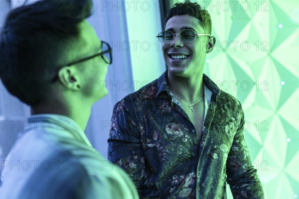 Two latin gay men smiling warmly at each other in an illuminated urban setting. Vibrant green tones