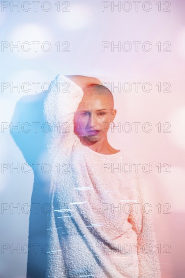 Middle-aged woman with shaved head poses confidently in creative lighting. The colorful bokeh