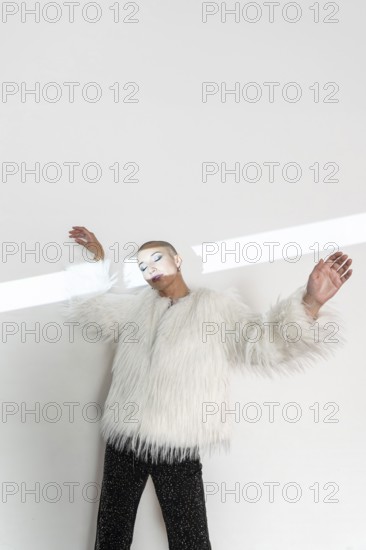 A middle-aged woman with a shaved head poses confidently in a luxurious white fur coat. The