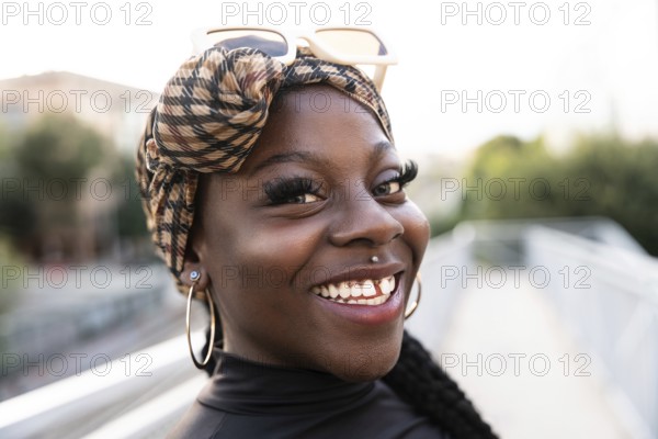 Vibrant portrait of a young black woman with a patterned headscarf and sunglasses, smiling brightly