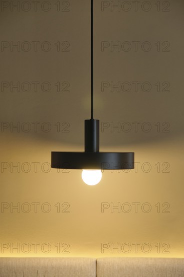 A modern hotel room showcases a sleek pendant light against a warm, neutral wall. The glowing bulb