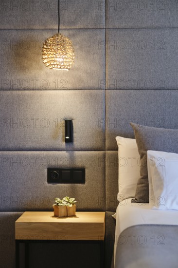 Elegant hotel room features a woven pendant light, modern upholstered wall, sleek bedside table