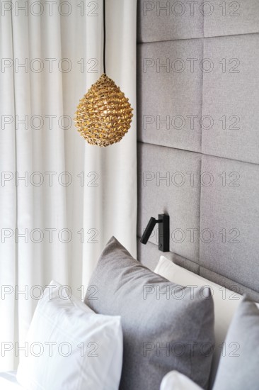 A cozy hotel room with a woven pendant lamp, plush gray pillows, and a textured gray upholstered