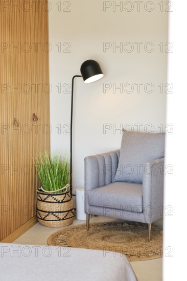 A cozy hotel room corner featuring a gray armchair, woven basket with green plant, and a sleek