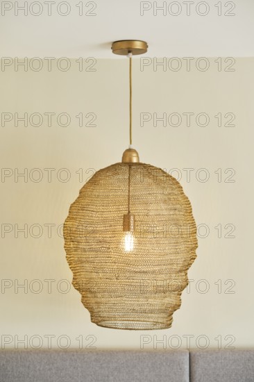 A stylish woven pendant light hangs from a hotel room ceiling, casting a warm glow. The beige color