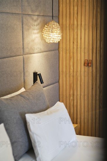 A modern hotel room features soft gray bedding, ambient pendant light, and vertical wood accents,