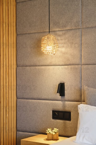 A serene hotel room with soft, woven pendant lighting, padded walls, and wooden accents, creating a