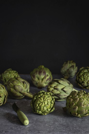 Fresh artichokes arranged artfully on a dark, textured surface, ideal for culinary and healthy