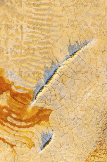 Aerial view of cracked mud in vibrant hues, showcasing an abstract pattern of orange, blue, and