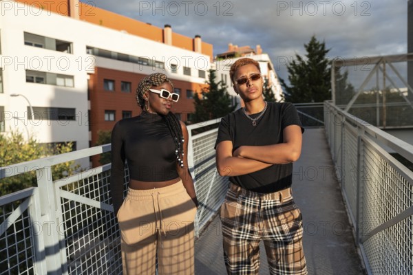 A stylish LGBT multiethnic couple poses confidently on an urban bridge under the warm, golden
