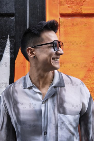 A stylish latin man wearing sunglasses and a patterned shirt smiles broadly against a vibrant