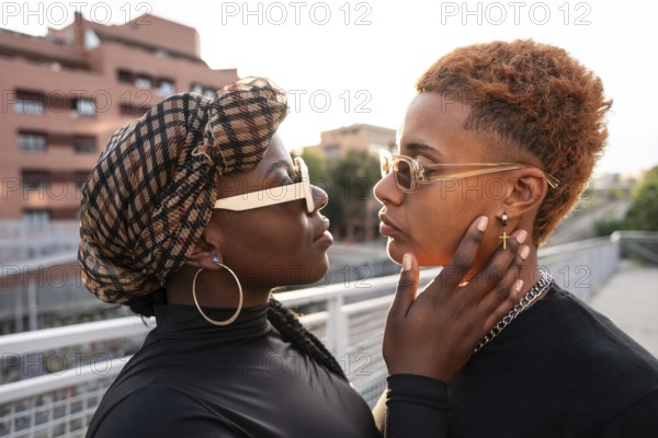 An LGBT multiethnic couple gazes into each other's eyes on a sunlit urban bridge, showcasing