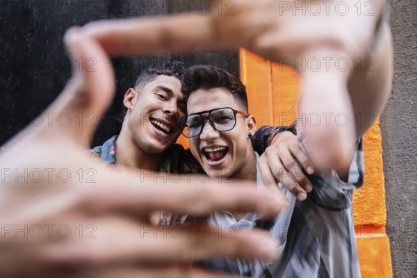 A smiling couple frames their joyful expressions with their hands against a vibrant orange urban