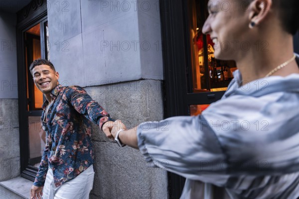 A smiling latin gay couple holds hands outside an urban cafe, radiating happiness and love. One