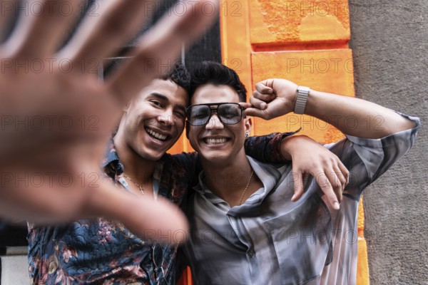 A smiling couple poses playfully in front of a bright orange wall. One partner playfully reaches
