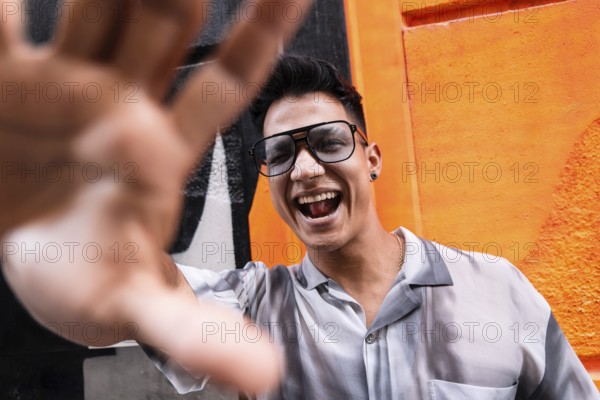 A young man wearing glasses and a stylish shirt smiles joyfully, extending his hand toward the