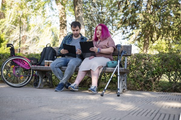 A college couple sits on a bench, studying with clipboards The woman, managing a disability due to