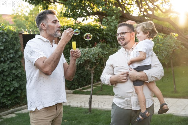 A heartwarming scene shows a gay couple cherishing playful moments with their son outdoors. One