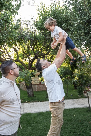 A loving gay couple enjoys quality time with their cheerful son in a lush garden setting. One