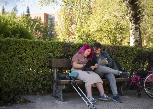 A couple studies together on a bench in a college garden The woman, with pink hair, uses a
